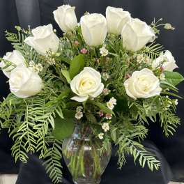 White roses arranged in a clear glass vase with mixed greenery