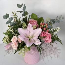 Pink roses and a pale lily arranged in a pink vase