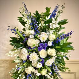 Tall standing spray of white and purple flowers with blue accents on a metal easel