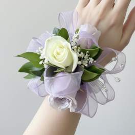 Lavender and white rose wrist corsage with ribbon and rhinestone accents on a person's hand.