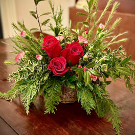 Low basket arrangement of red roses and small pink flowers with abundant evergreen foliage