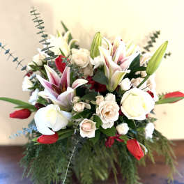 Arrangement of white roses, blush lilies, and red tulips in a clear vase with cascading greenery.