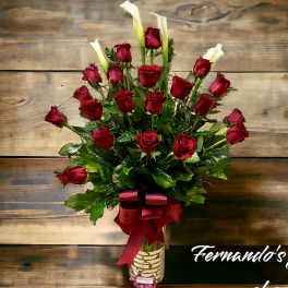 Tall arrangement of red roses and white calla lilies in a clear glass vase with a red bow