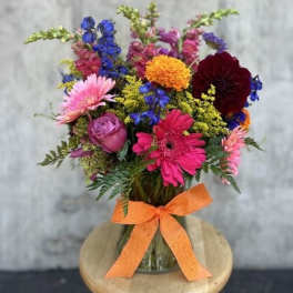 Mixed bouquet of colorful flowers in a glass vase with an orange ribbon