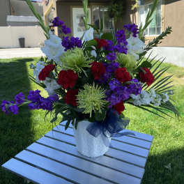Large mixed floral arrangement in a white vase with purple, red, and white blooms