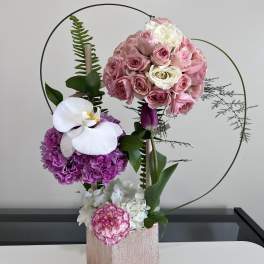 Pink and white floral arrangement in a rose-gold box with circular wire accents.