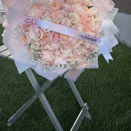 Large bouquet of pale pink roses wrapped in pink paper with a ribbon