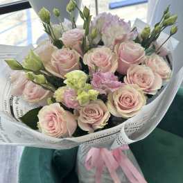 Bouquet of pale pink roses and lisianthus wrapped in paper with a pink ribbon