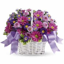 Purple and pink daisy bouquet in a white wicker basket with lavender ribbon