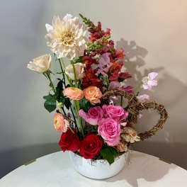 Mixed bouquet of roses, ranunculus, and snapdragons in a white bowl vase