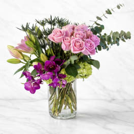 Pink roses and purple orchids in a clear glass vase