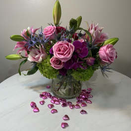 Pink roses and lilies arranged in a glass vase with heart confetti