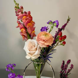 Mixed flowers arranged in a clear vase with small accent vases on a table