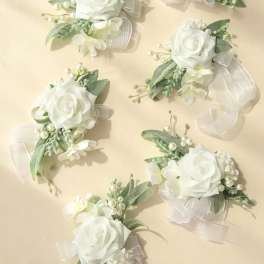 Set of white rose and pearl corsages with sheer white ribbon on a light beige background