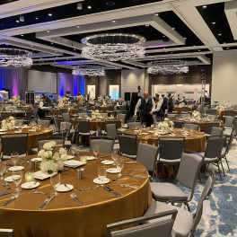 Large banquet hall with round tables and low white floral centerpieces.