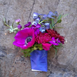 Small bouquet of magenta, red, and blue flowers wrapped in blue paper