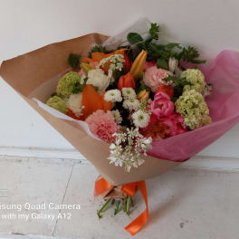 Mixed bouquet of orange, pink, and white flowers wrapped in brown paper