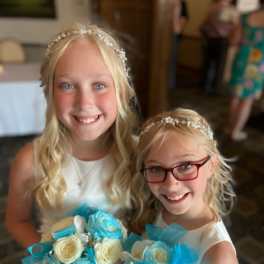 Two girls in white dresses holding small blue and white rose bouquets