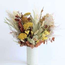 Tall dried-style arrangement with yellow and rust flowers in a white cylindrical vase