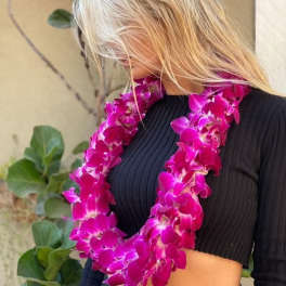 Woman wearing a bright pink orchid lei over a black top