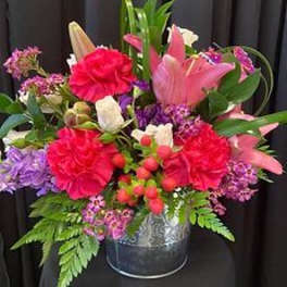 Mixed bouquet of pink lilies, carnations, and purple flowers in a metal vase