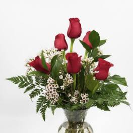 Red roses arranged in a clear glass vase with small white filler flowers