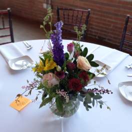 Mixed floral centerpiece in a clear glass bowl on a white tablecloth