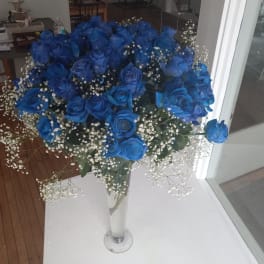Blue roses in a tall glass vase with white baby's breath