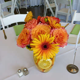 Orange and yellow flower arrangement in a glass vase with citrus slices