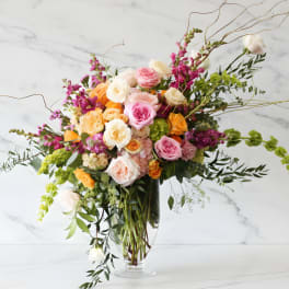 Large mixed bouquet of pink, peach, white, and yellow flowers in a clear glass vase
