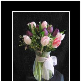 Pink and purple tulips in a clear vase with a white ribbon
