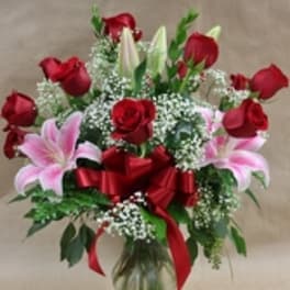 Bouquet of red roses and pink lilies in a glass vase with a red ribbon
