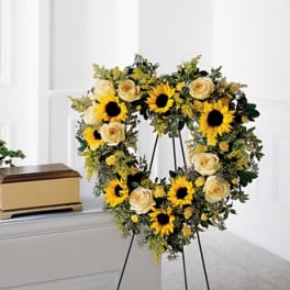 Heart-shaped floral wreath with sunflowers and cream roses on a stand