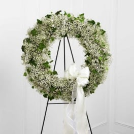 White floral wreath on a black stand with a white ribbon bow