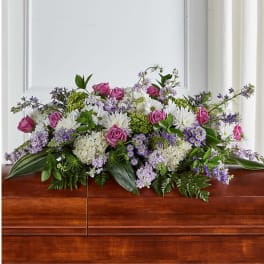 Casket spray with pink roses, white flowers, and purple accents