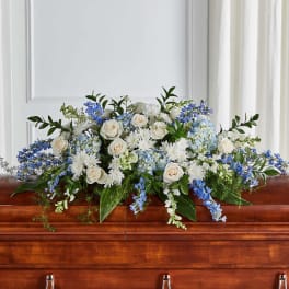 White and blue casket spray with roses and delphinium on a wooden casket
