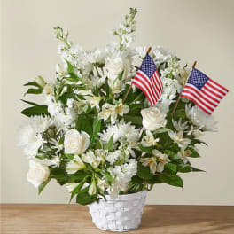 White floral arrangement in a white basket with two small American flags
