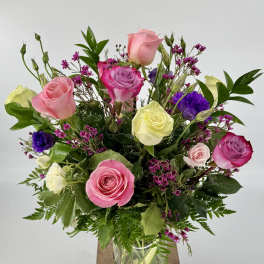 Mixed bouquet of pink, purple, and yellow roses in a glass vase