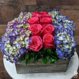 Pink roses surrounded by blue-purple hydrangeas in a wooden box