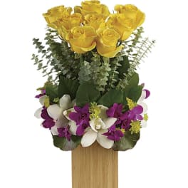 Tall arrangement of yellow roses with purple and white orchids in a rectangular wooden vase.