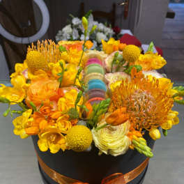Orange and yellow floral arrangement in a black hatbox with ribbon