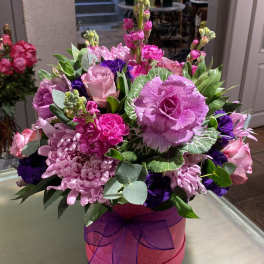 Pink and purple mixed flower arrangement in a round hatbox with ribbon
