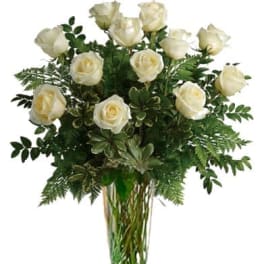 White roses arranged in a tall clear glass vase with greenery