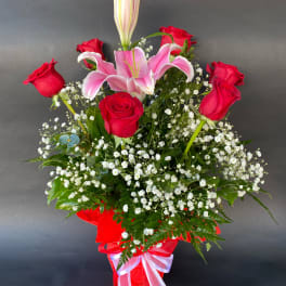 Red roses and pink lilies in a red ribboned vase arrangement