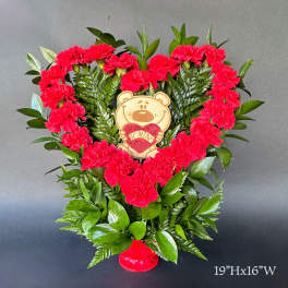 Heart-shaped carnation arrangement with a teddy bear topper