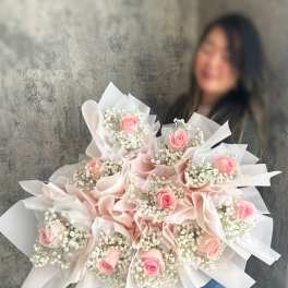 Large bouquet of pink roses and white baby's breath wrapped in pale paper