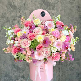 Large pink floral arrangement in a round pink box with a lace ribbon