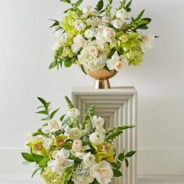 Two white and green floral arrangements in gold pedestal vases