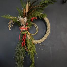 Holiday greenery arrangement with red berries and a braided straw ring