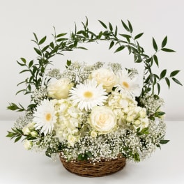 White roses and daisies in a wicker basket with a leafy arch